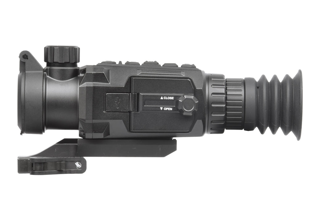 A thermal scope with a black polymer frame and red reticle, mounted on a rifle, showing heat signatures of targets in a woodl