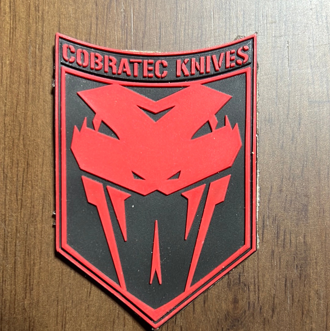 A green and black CobraTec patch with a reflective logo on a dark background by CobraTec.